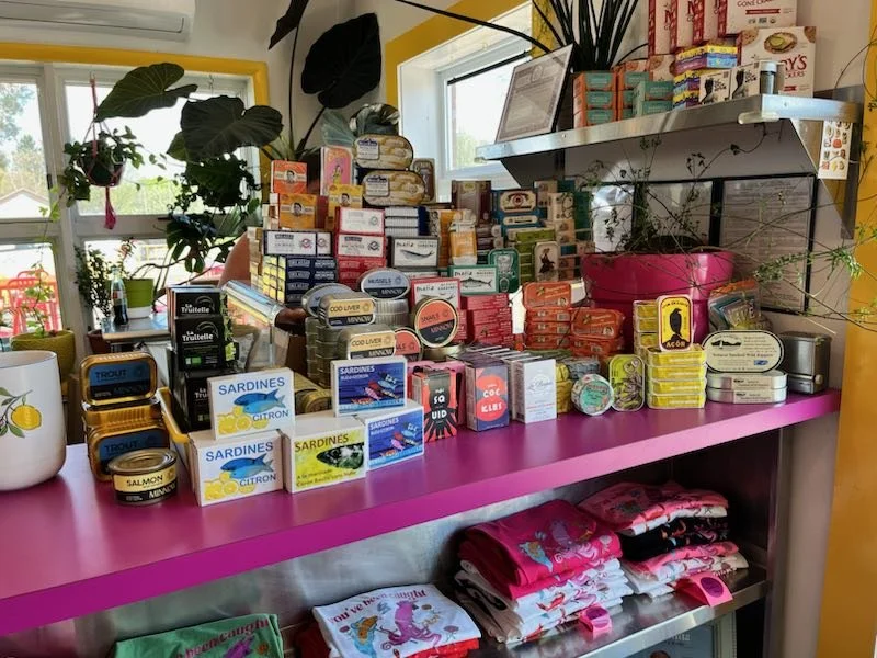 Tinned fish stacked on the magenta shelf by the window