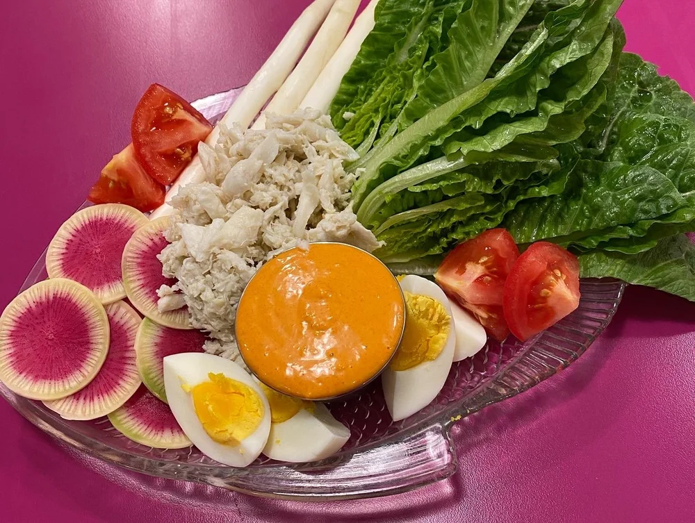 A crudité plate with watermelon radish, romaine, egg and tomato on the pink counter